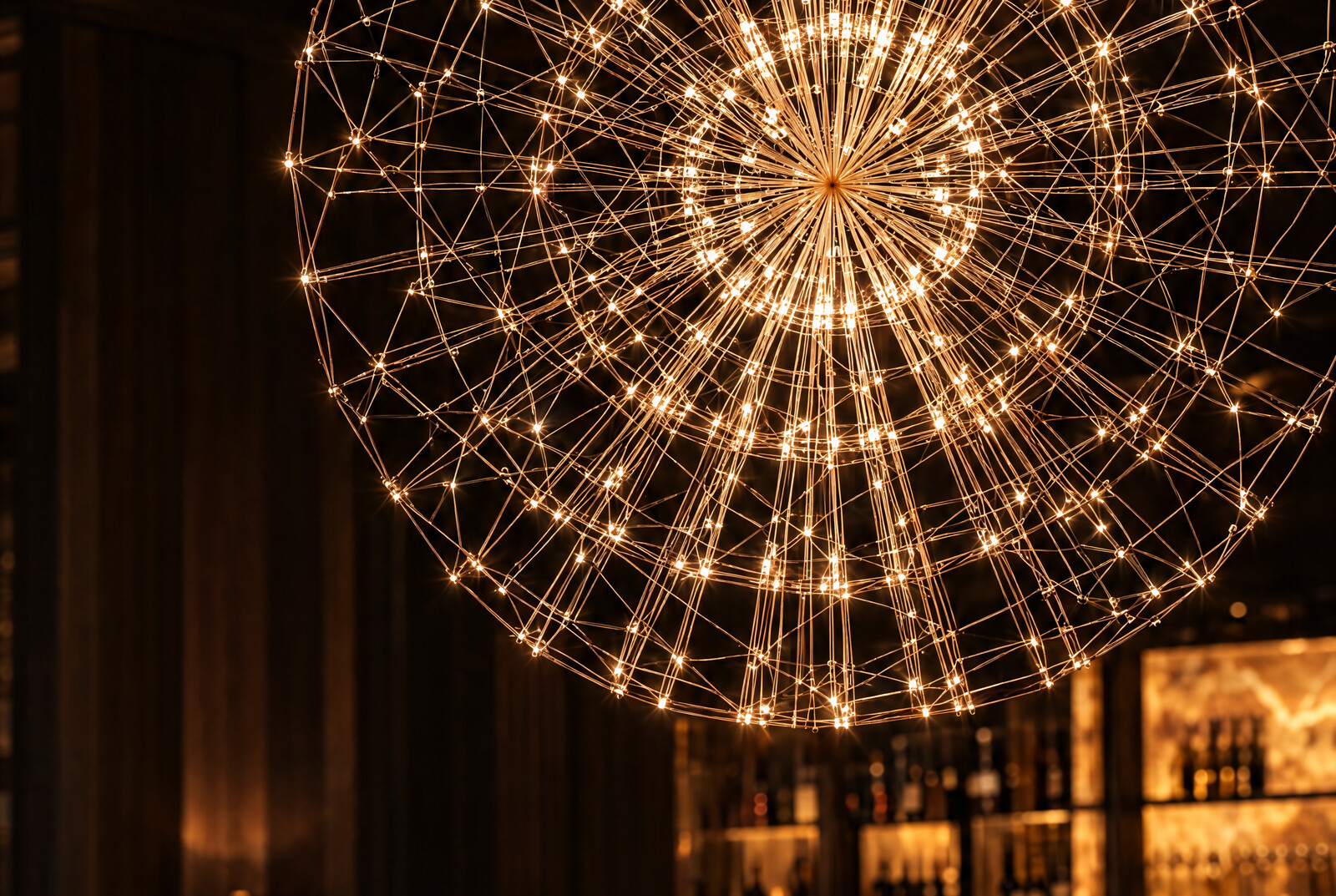 Pyrox Lux chandelier above an intimate bar, backlit marble shelving and warm amber light